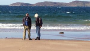 Two people with their backs on the camera look out over Loch Ewe from Firemore beach
